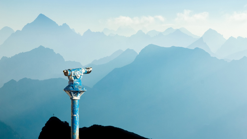 Public binoculars provide far view to distant blue mountain ranges silhouette in early Morning Sunlight.