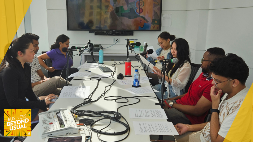 Group of people seated around a table with microphones, participating in a podcast or panel discussion.