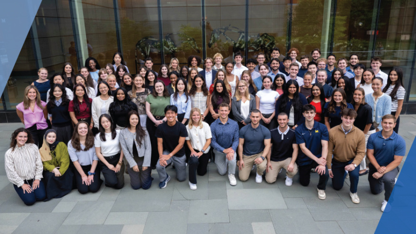 Large group of people posing together outside a modern glass building.