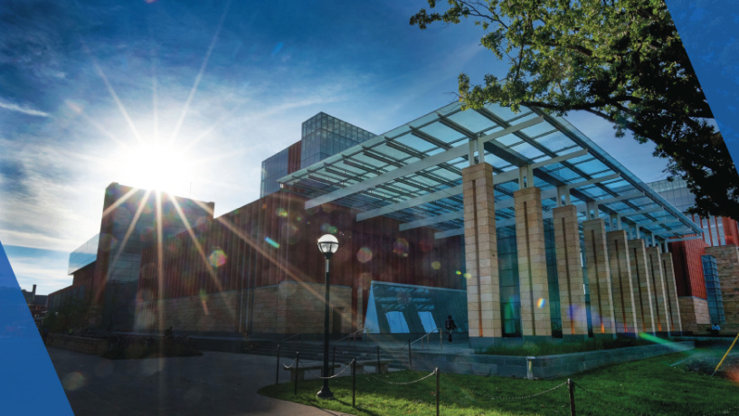 Modern glass-fronted building with sunlight streaming through, set against a blue sky.