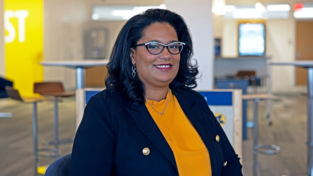 A woman in business attire smiles while seated in a modern office space.