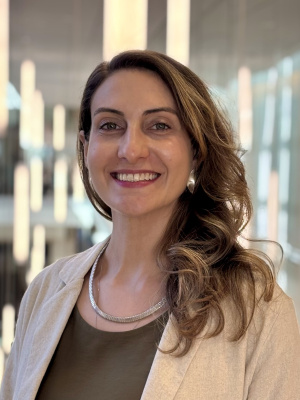 Isadora is smiling, wearing a beige blazer and dark green blouse.