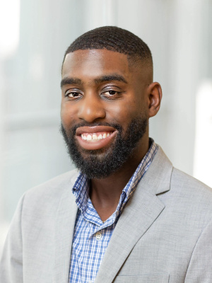 Photo of Nick Shepard wearing a blue shirt and grey suit.  He is African American with short hair