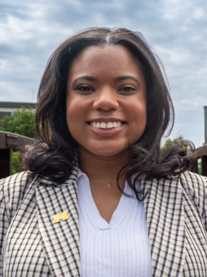 African American Women in plaid blazer with white shirt outside on a sunny day with clouds. 