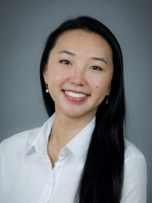 Woman with black hair and white shirt against gray background.