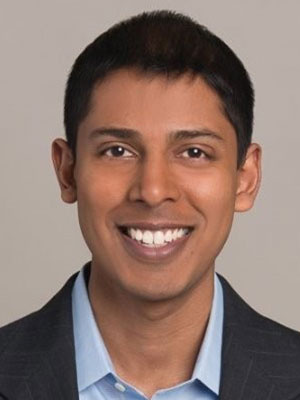 Annaad Christopher wearing a suit jacket and light blue shirt against a neutral background.