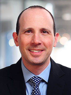 Seth Katzenstein in a suit and tie smiling in an office setting.