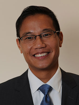 Alfonso Chang wearing glasses and a suit smiling at the camera.