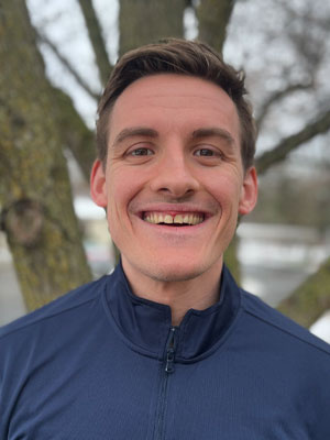 Headshot of Riley VanPelt - smiling outdoors with trees in the background.