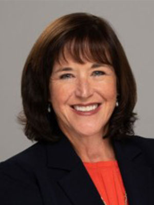 Kerry Philipovitch with shoulder-length brown hair wearing a dark blazer and orange top.