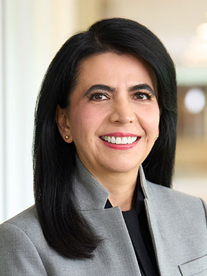 Pilar Cruz with long dark hair smiles, wearing a light gray blazer in a professional setting.