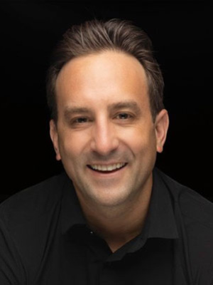 Brian Lafer smiling in front of a dark background.