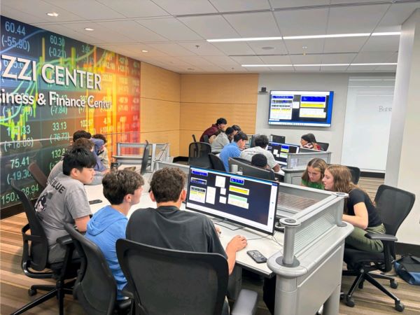 Students sit around a desk with multiple monitors working with investing software/