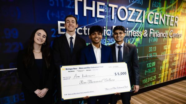 Four students pose with a giant check in the Tozzi Finance Center