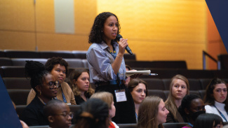 A woman standing in a small crowd speaking into a microphone