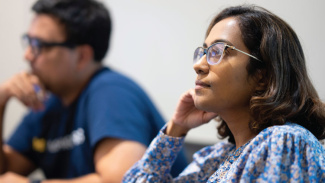 Two people sitting at desks thinking and staring at something out of frame.