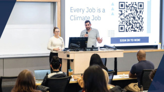 Two students stand behind a desk presenting information to a class of peers
